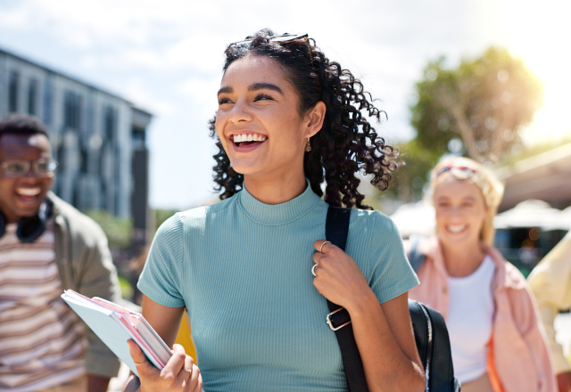 female student on campus holding books and nap sack with male and female friends smiling behind