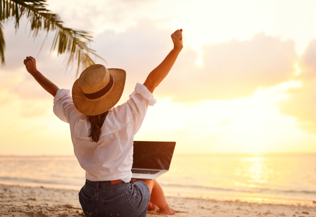 girl with hat and laptop celebrating on the beach with sunset and palm tree fronds
